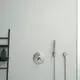 Einzelthermostat von Ideal Standard, installiert an einer hellen Wand. Enthält eine Steuerung und eine Handbrause mit Halterung. Daneben ein schwarzes Regal für Pflegeprodukte.